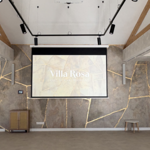 Salle événementielle – écran de projection motorisé Écran de projection motorisé intégré au volume existant de la grande salle. Les enceintes colonnes, disposées de part et d'autre, assurent une restitution sonore homogène pour les séminaires et événements. L'ensemble se rétracte en plafond hors utilisation, sans impact sur l'esthétique du lieu.