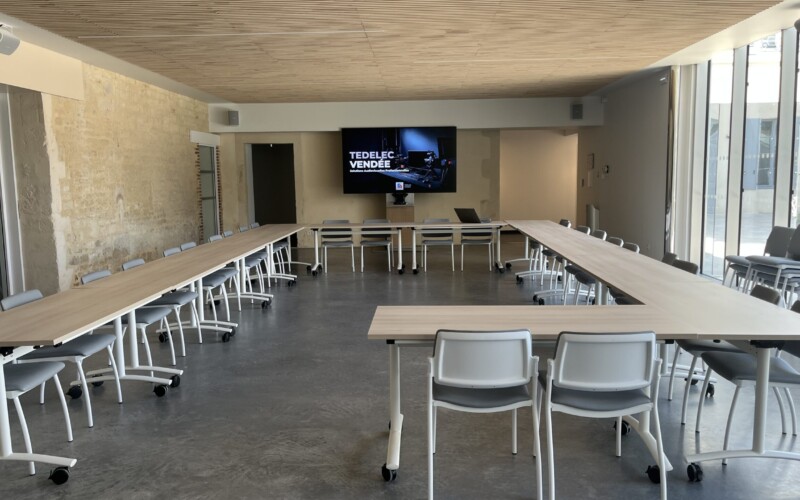 Grande salle de réception en configuration en U : écran Samsung QM98C sur pied AXEOS, enceintes Bose DesignMax en façade et caméra AVer CAM570 — intégration audiovisuelle assurée par Tedelec Vendée. Grande salle de La Distylerie de Luçon en configuration U, écran Samsung QM98C et enceintes Bose intégrés par Tedelec Vendée